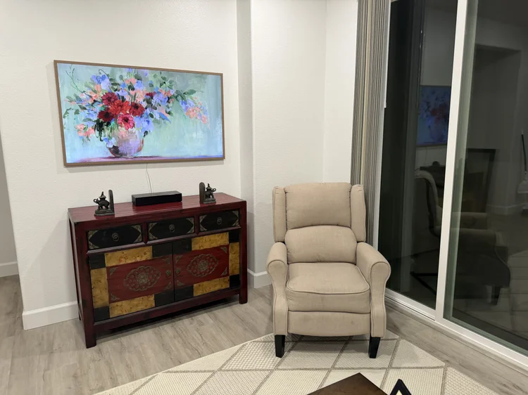 A floral canvas above a red cabinet, beside a reading chair.