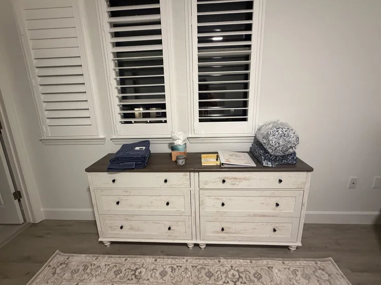 A dresser beneath two shuttered bedroom windows.