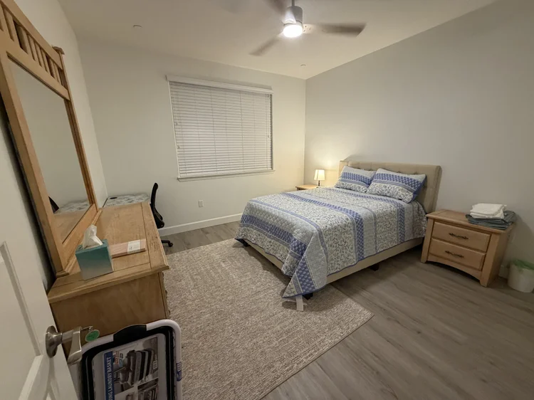 A bedroom with a mirrored dresser and a desk by the window.